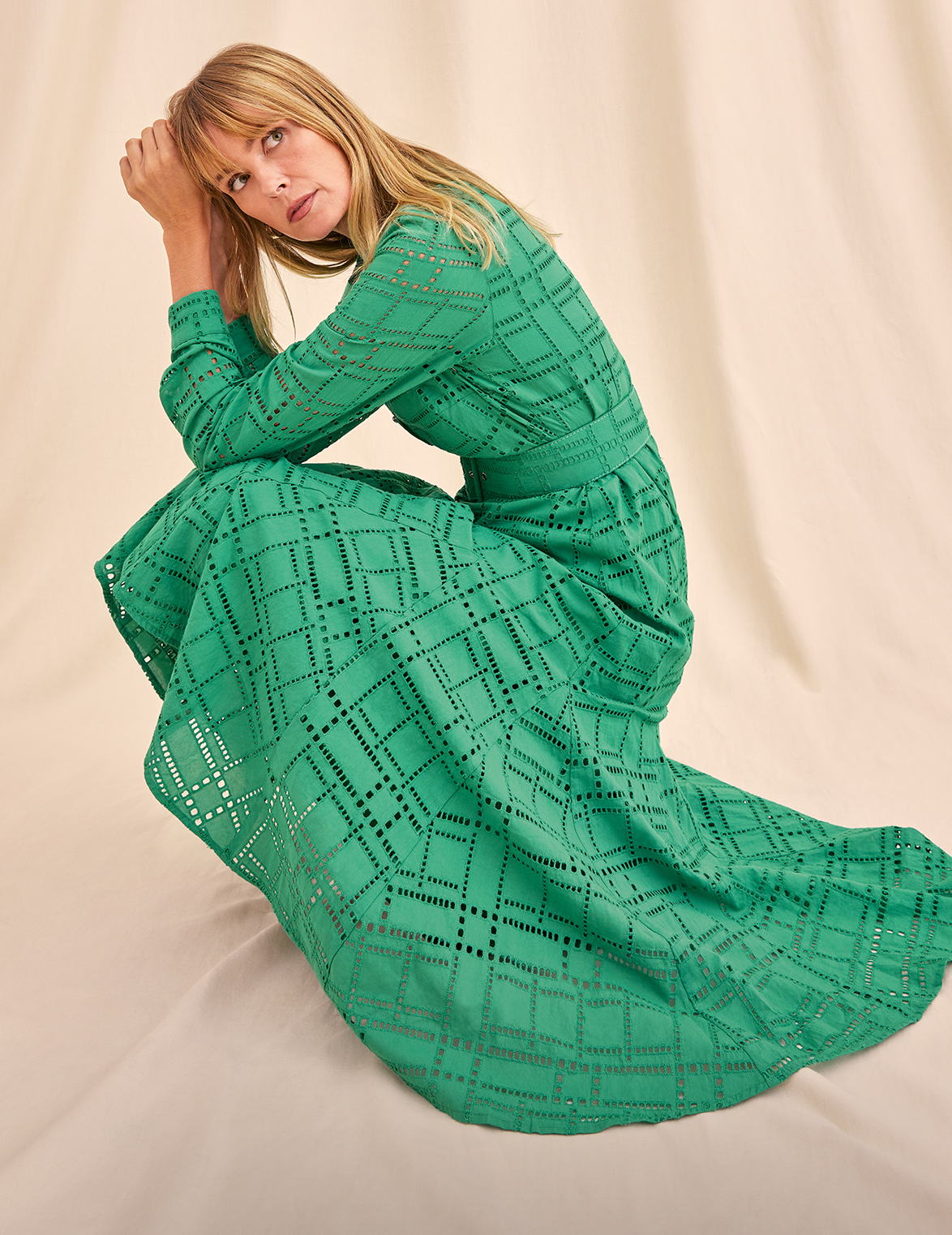Woman looking away, in a bright green, long-sleeved broderie midi dress