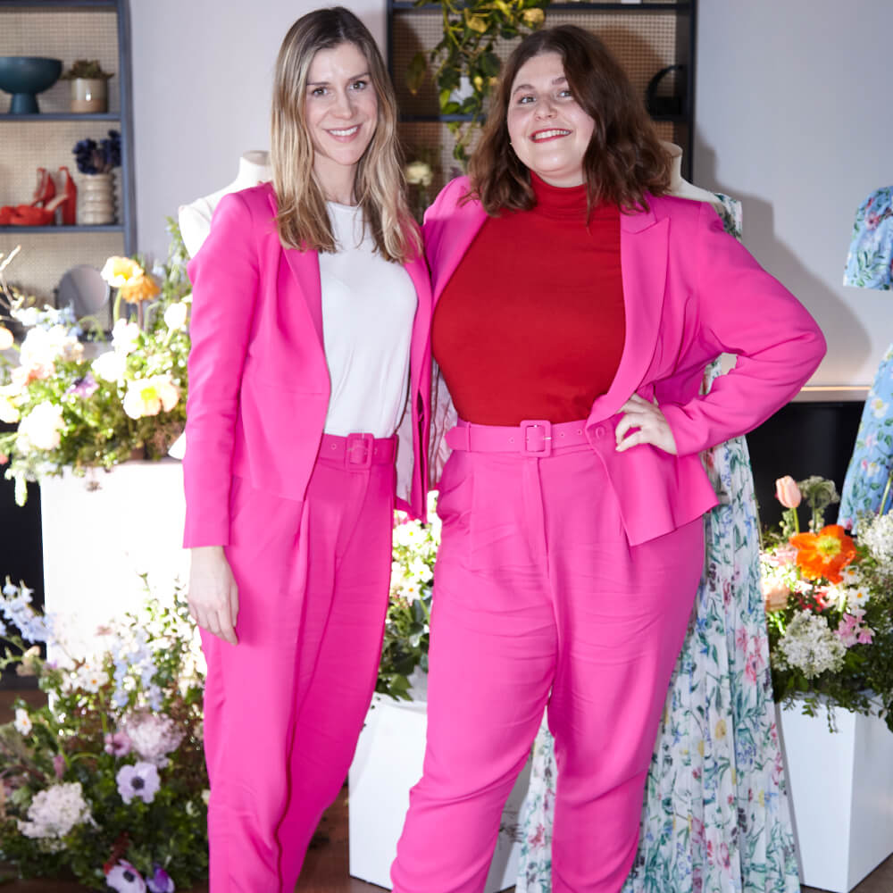 Two women wearing pink blazer and pink trousers