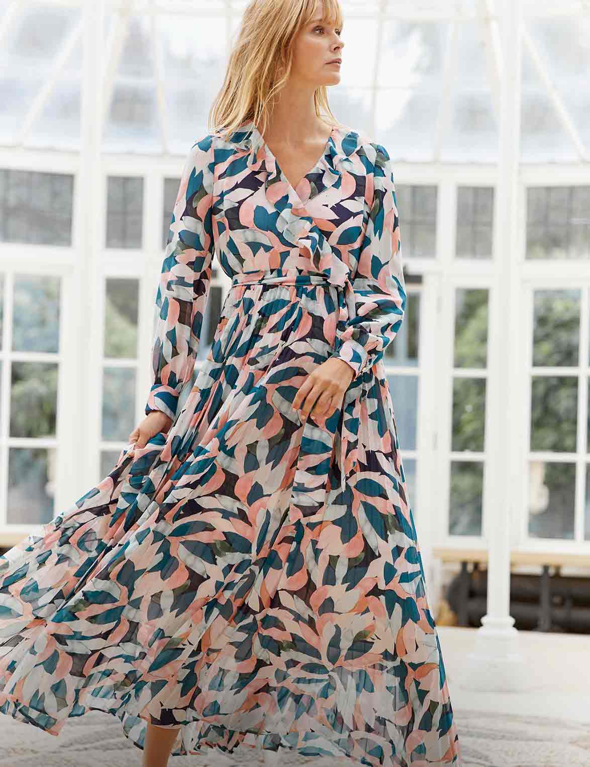 Woman looking to her left in a pink and blue patterned, long sleeve maxi dress