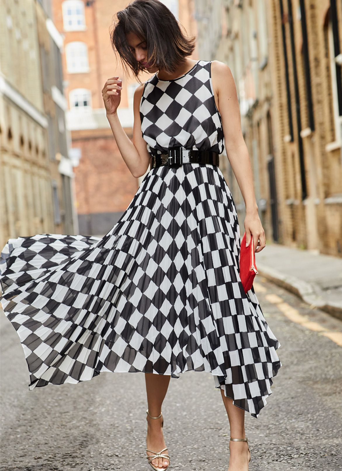 Woman looking down in black and white check occasion dress with bright red bag