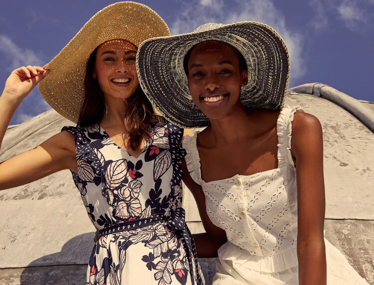 Two women wearing summer dresses and straw hats